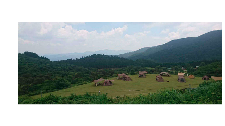 広い芝生の上にテントが並ぶスノーピーク奥日田キャンプ場の風景。周囲は緑の山々に囲まれ、リラックスできる自然豊かな環境。